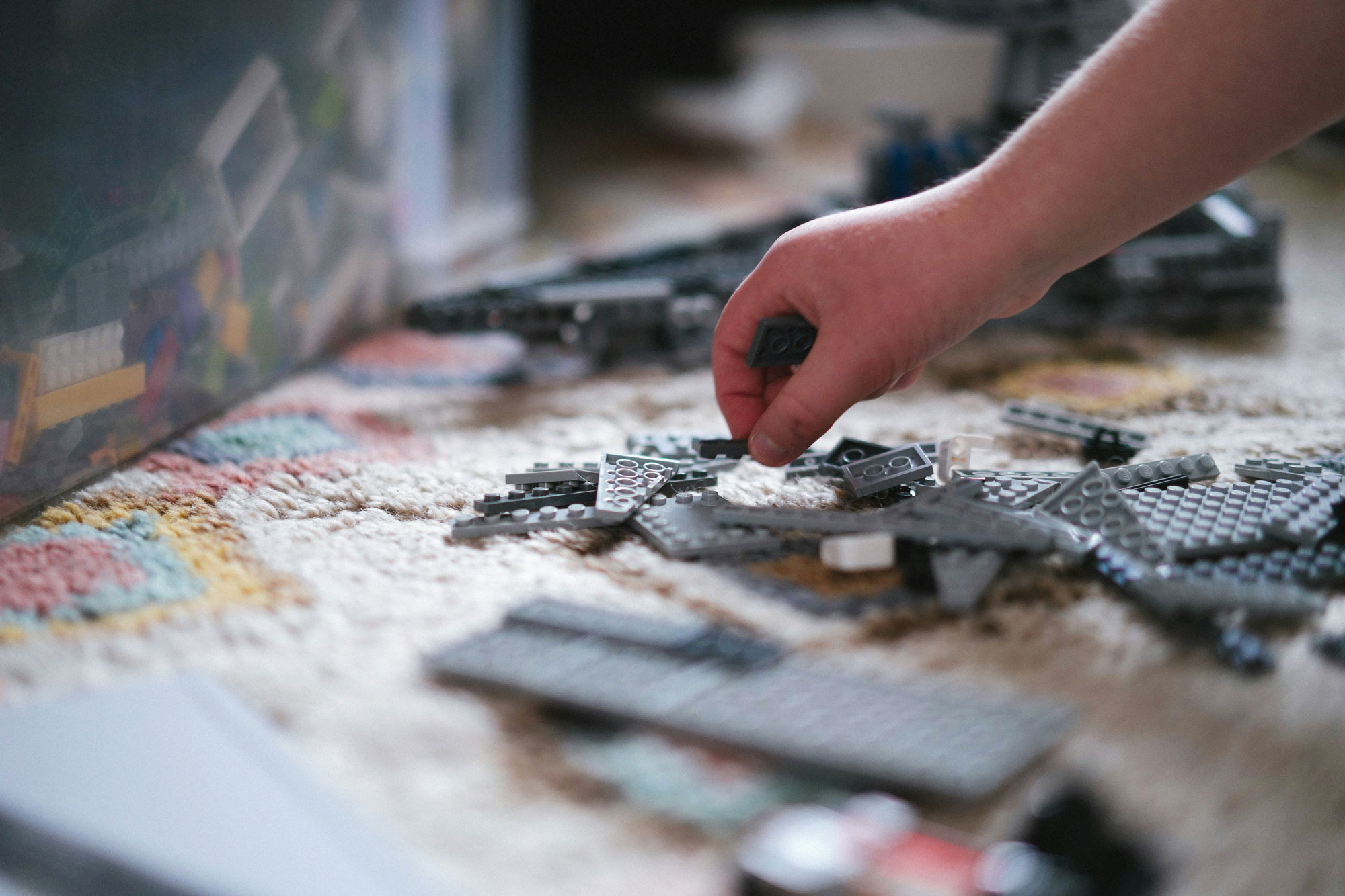 A child's hand reaching out and choosing a lego piece among a pile of grey lego bricks.